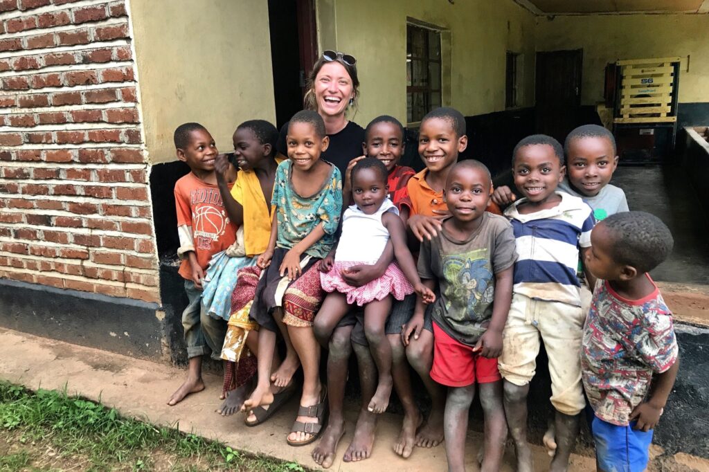 A photo of Jenna sitting between a group of African school children, all smiling at the camera.